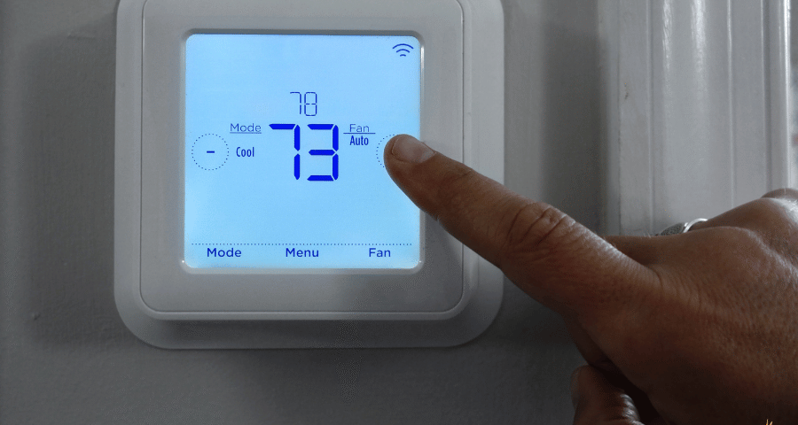 Homeowner adjusting smart thermostat mounted on wall